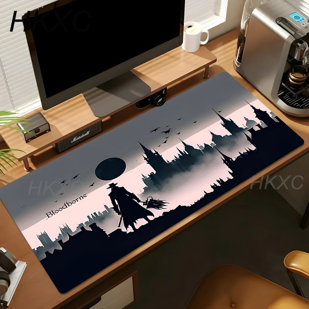 A large rectangular desk mat with a dark fantasy cityscape and character design, placed on a wooden desk in a home office setup next to a computer monitor, coffee machine, and mug.