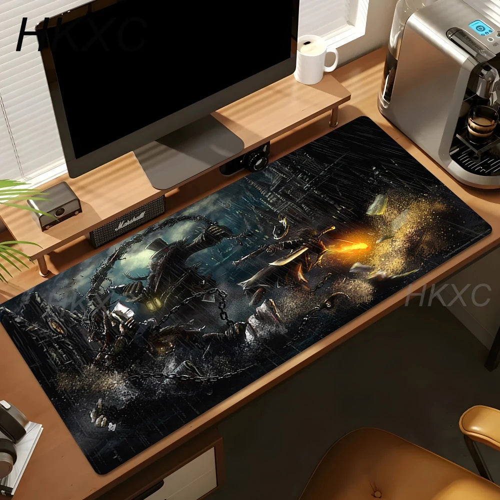 A large rectangular desk mat with a dark sci-fi battle scene print, shown on a wooden desk in a home office setup with a computer monitor, coffee machine, and mug.
