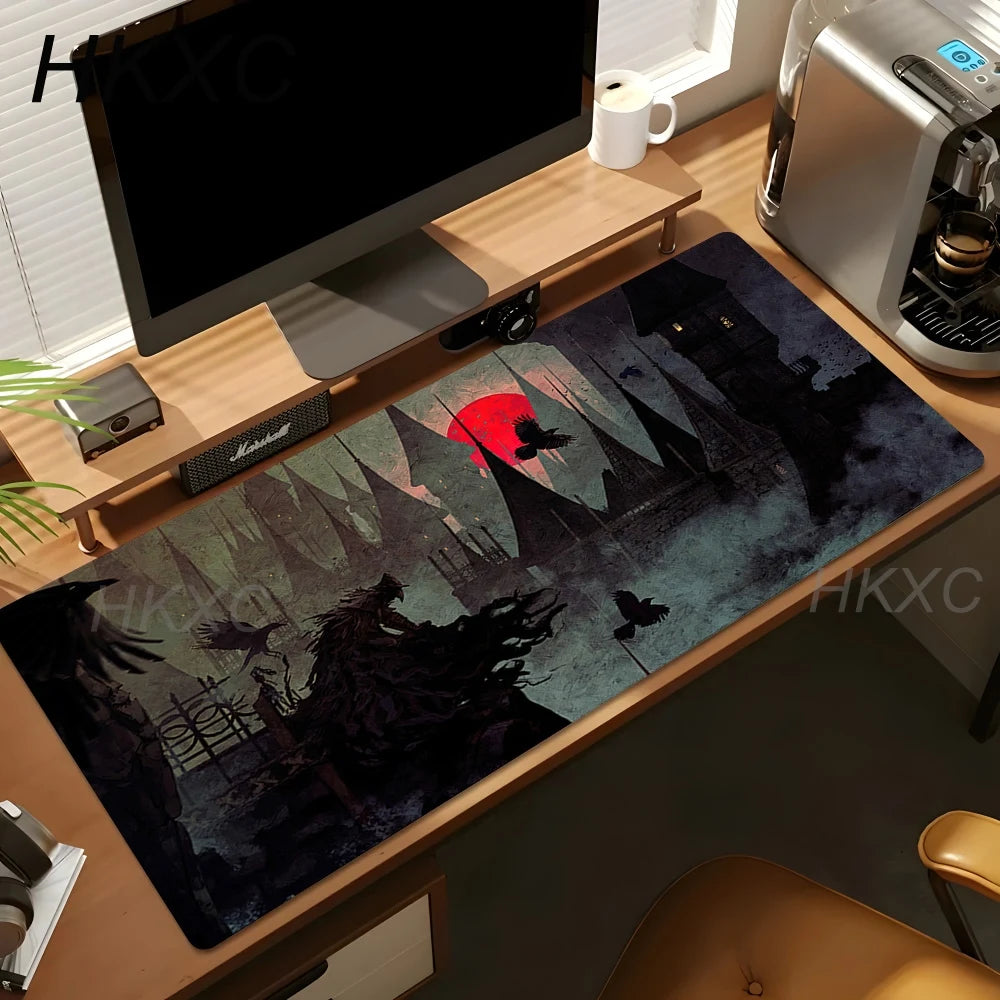 A large rectangular desk mat with a dark fantasy castle scene and a red sun, shown on a wooden desk next to a computer monitor, coffee machine, and mug.