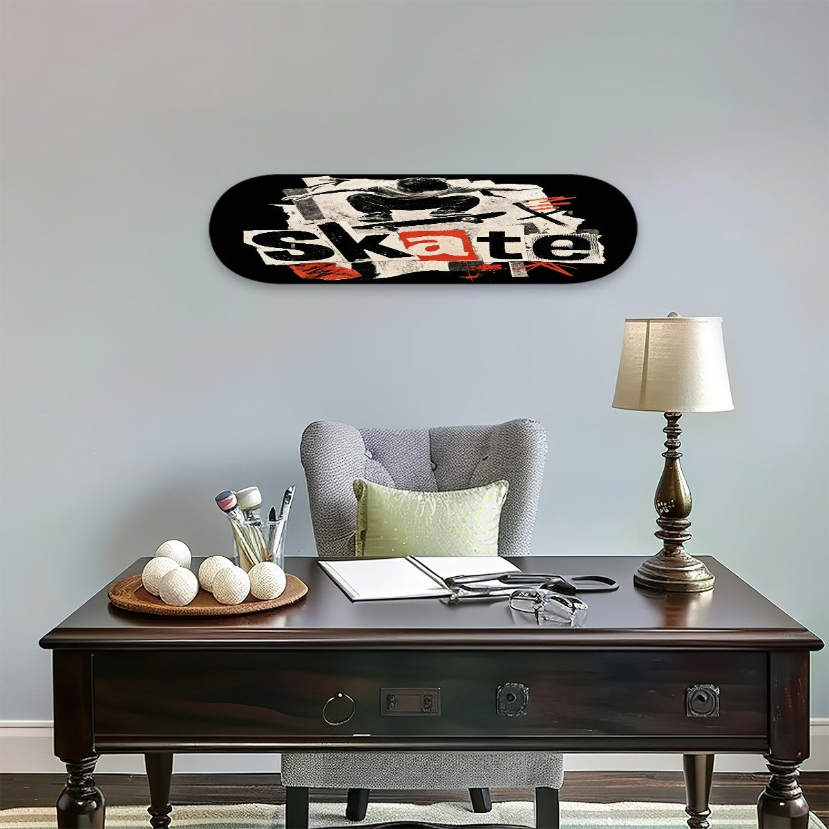 A skateboard wall art print featuring a graphic collage with the word 'Skate' in white and orange, displayed in a styled home office setting above a dark wood desk with a gray armchair and a table lamp.