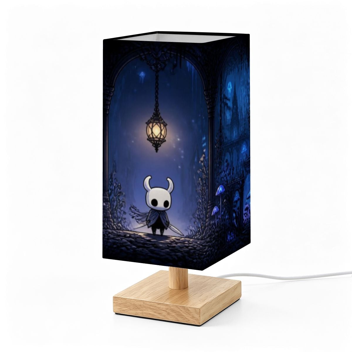 A square table lamp with a light wood base and a dark blue printed shade featuring a whimsical character scene under a hanging lantern, shown on a white background.